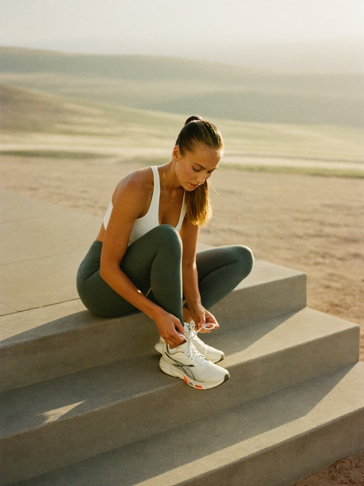 A woman lacing running shoes on her front steps at sunrise