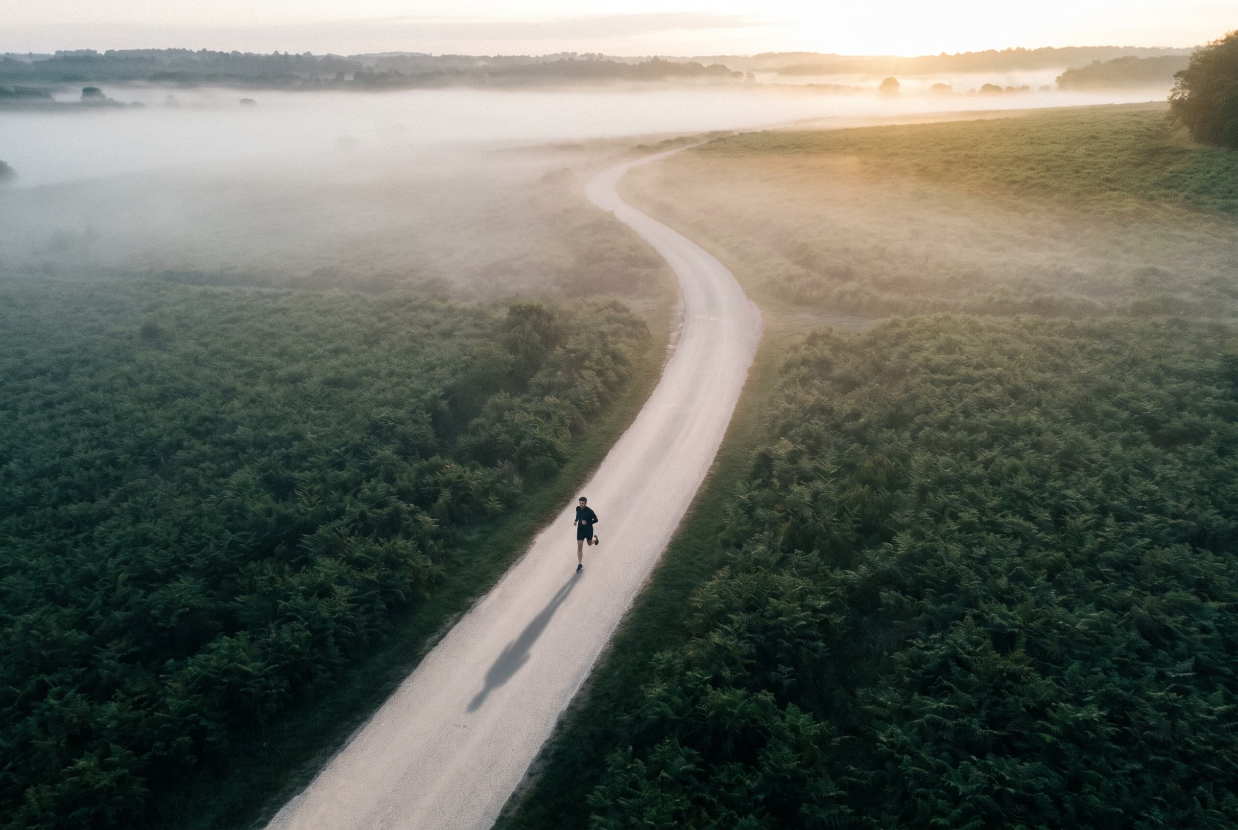 A lone runner on a misty winding road at dawn, seen from above